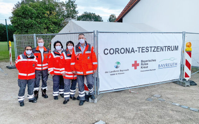 Ehrenamtliche RotKreuzler errichten Schnelleinsatzzelt zum Schutz vor Regen und Wind am Corona-Testzentrum in Bayreuth.