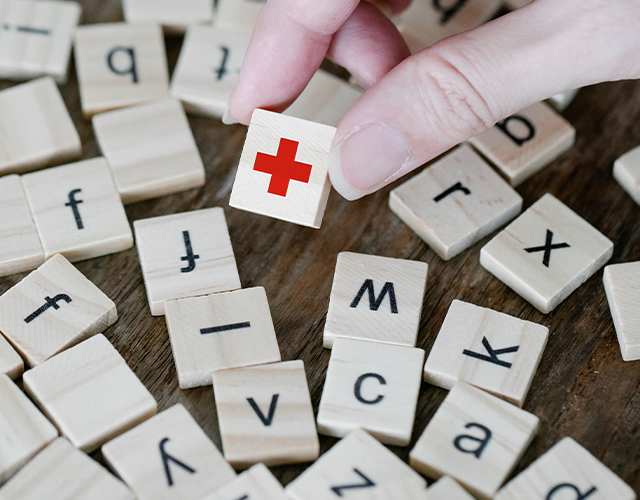 Holzbuchstaben mit Buchstaben auf dem Tisch und eine Hand hebt ein Holzstein mit einem roten Kreuz hoch
