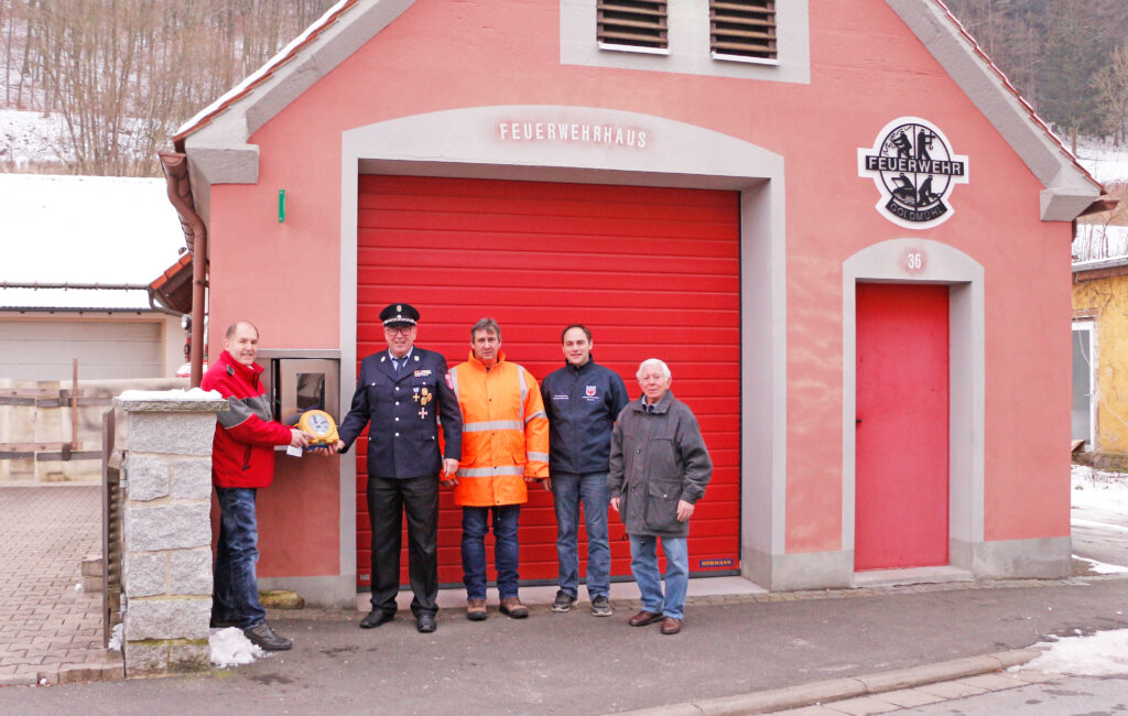 Feierliche Inbetriebnahme des öffentlich-zugänglichen Defis Am Feuerwehrhaus in Goldmühl (bei Bad Berneck). Im Bild (v.l.n.r.): Karl Bernet (Projektkoordinator Defi-Netzwerk Bayreuth, BRK Bayreuth), Robert Fischer (Vorsitzender der Feuerwehr Goldmühl und zweiter Bürgermeister Bad Berneck), Kommandant der Feuerwehr Goldmühl, Christian Heidenreich (Kreisbrandmeister Kreisfeuerwehr Bayreuth) und Heinz Zahn (Vorsitzender Heimat und Trachtenverein Goldmühl).