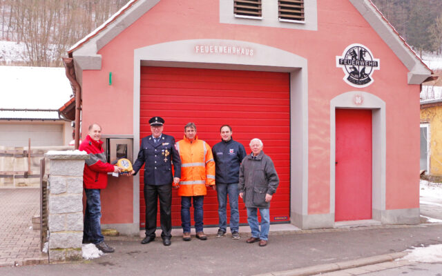 Feierliche Inbetriebnahme des öffentlich-zugänglichen Defis Am Feuerwehrhaus in Goldmühl (bei Bad Berneck). Im Bild (v.l.n.r.): Karl Bernet (Projektkoordinator Defi-Netzwerk Bayreuth, BRK Bayreuth), Robert Fischer (Vorsitzender der Feuerwehr Goldmühl und zweiter Bürgermeister Bad Berneck), Kommandant der Feuerwehr Goldmühl, Christian Heidenreich (Kreisbrandmeister Kreisfeuerwehr Bayreuth) und Heinz Zahn (Vorsitzender Heimat und Trachtenverein Goldmühl).