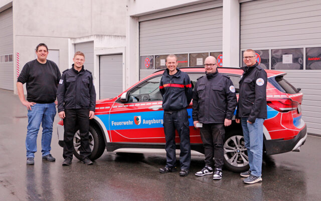 DIe Kollegen der Augsburger Feuerwehr und der TTB der Integrierten Leitstelle Bayreuth Kulmbach beim Besuch in Bayreuth vor einem Dienstfahrzeug der Feuerwehr Augsburg.