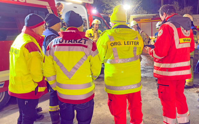 Leiter der Einsatzkräfte beim Briefing am Einsatzort. Im Hitnegrund Einsatzfahrzeuge der Feuerwehr.
