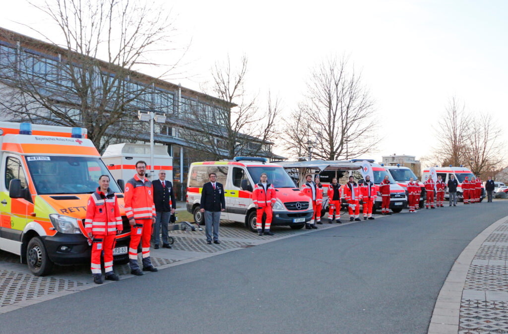 Das Bild zeigt die Fahrzeugausstellung der neu angeschafften oder instandgesetzten Einsatzfahrzeuge der Gemeinschaften des BRK-Kreisverbandes Bayreuth vor der Bärenhalle in Bayreuth. Darunter zwei Rettungsboote, ein Notstromaggregat, mehrere Mannschaftstransporter, ein Rettungswagen und eine Feldküche.