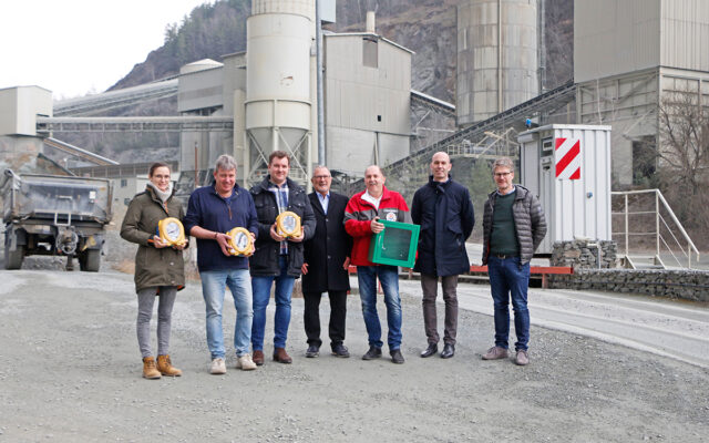 Im Bild zu sehen: Valentina Schicker (Geschäftsführende Gesellschafterin), Otto Kreil (Technischer Leiter Firmengruppe Schicker), Daniel Schmidt (Geschäftsführer Verwaltungsgesellschaft Schicker), Bürgermeister Jürgen Zinnert, Karl Bernet (Projektkoordinator Defi-Netzwerk Bayreuth), Philipp Vogler (Geschäftsführer Steinlando) und Bernhard Leutheußer (Geschäftsführer Hartsteinwerke Schicker) mit Defibrillatoren in den Händen. Im Hintergrund das Steinwerk der Firma Schicker in Bad Berneck.