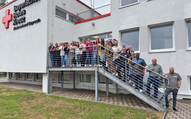 Teilnehmende der Schulung Internationale Fachkräfte: Chance und Herausforderung mit Dozentin Priscilla Hirschhausen und Ibukun Koussemou vor der Geschäftstelle des BRK Bayreuth. (Gruppenfoto)