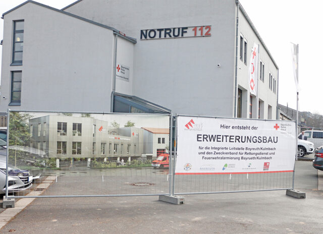 Startschuss für den Erweiterungsbau der ILS Bayreuth/Kulmbach. Aufnahme vor dem bestehenden Gebäude mit Illsutration des neuen Gebäudes.