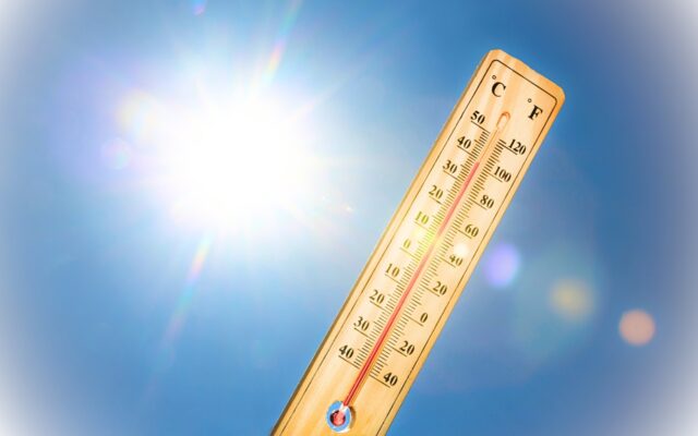 Thermometer vor blauem Himmel und Sonne.