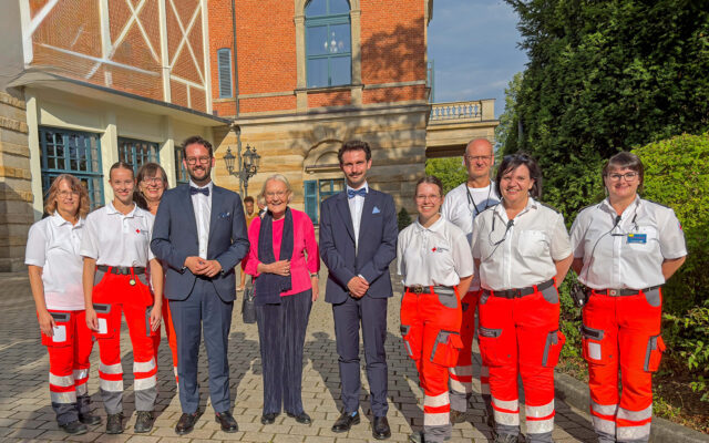 Im Bild: Die Kameradinnen und Kameraden der BRK-Bereitschaft Bayreuth bei der Absicherung der Bayreuther Festspiele, mit Oberbürgermeister Andreas Zippel. Im Hintergrund das Bayreuther Festspielhaus.