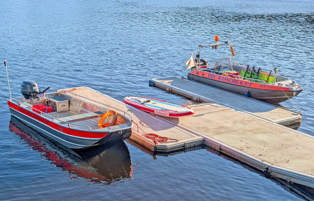 Wasserrettungsmittel der Wasserwacht am Fichtelsee, bereit zum Einsatz. Zu sehen sind 2 motorbetreibene Rettungsboote der Wasserwacht und ein Rettungs-Surfbrett. Alle drei Wasserfahrzeuge liegen an einem Steg bereit, für den Notfalleinsatz.